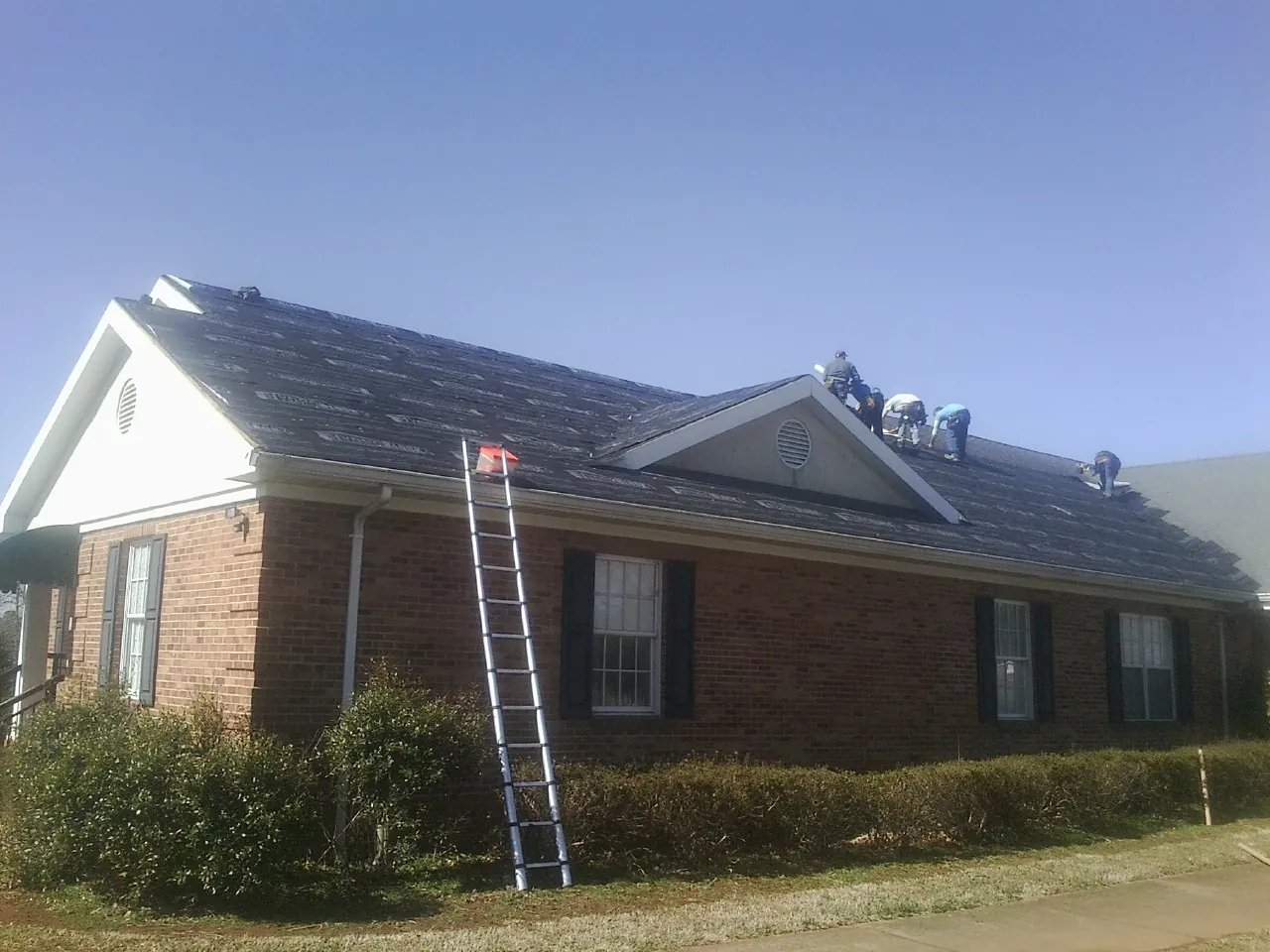 Crew tearing shingles off a brick ranch roof with a ladder set — Emergency Roof Repair work by our crew in Yachats