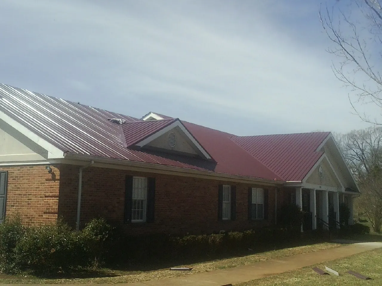 Red metal roof with gabled entries on a long brick building, from a Hail Damage Roof Repair job in Yachats