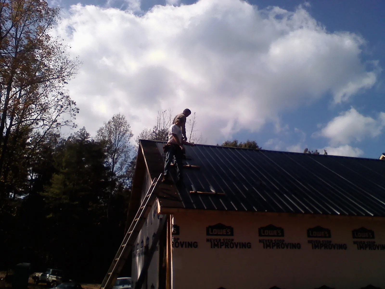 Roofer fastening dark metal panels high against a cloudy sky, from a Roof Inspection job in Yachats