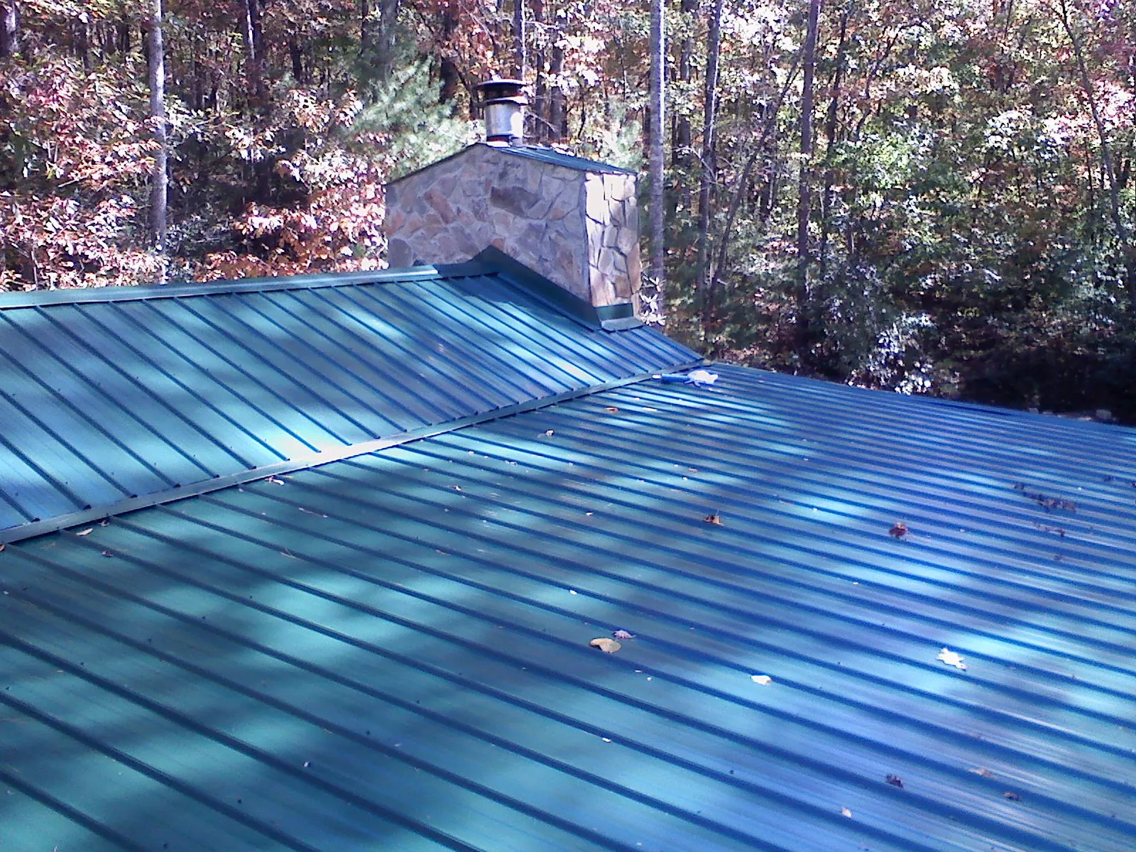 New green metal roof and stone chimney surrounded by autumn woods in Yachats